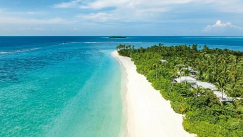 Luftaufnahme der üppig bewachsenen Privatinsel mit langem Sandstrand und türkisblauer Lagune im Raa-Atoll