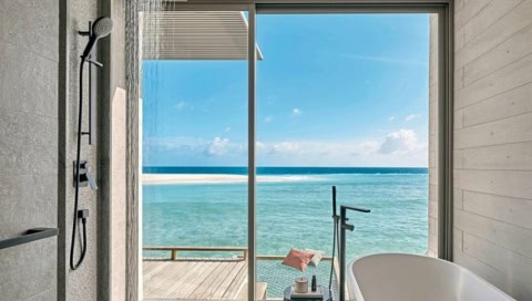 Badezimmer der Sunset Overwater Villa mit bodentiefer Fensterfront und Blick auf den Ozean