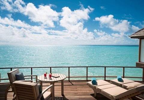 Private Terrasse einer Overwater-Villa mit Sonnenliegen und Blick auf den Indischen Ozean.