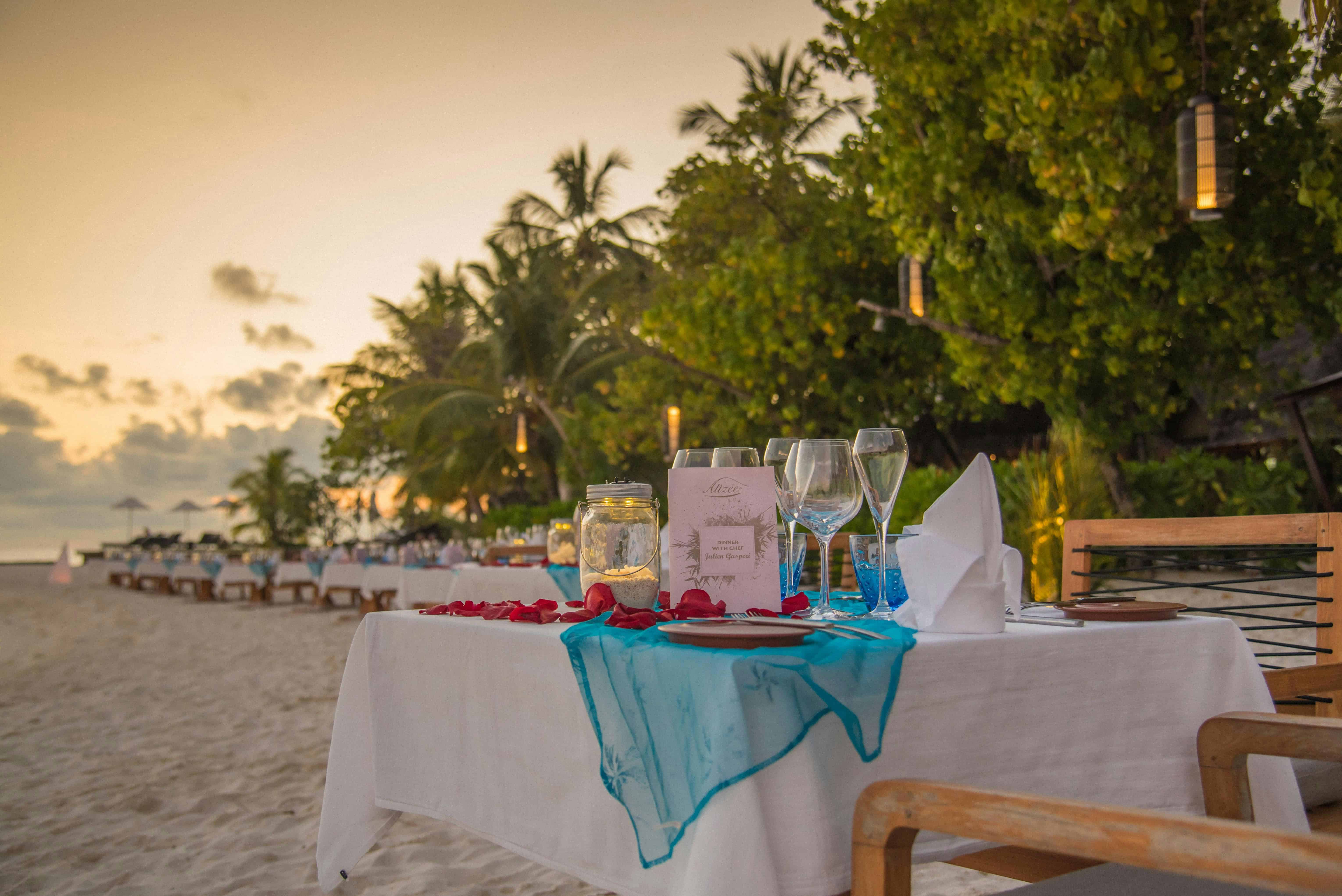 Romantisch gedeckter Tisch am Strand bei Sonnenuntergang mit Kerzen und Meerblick für ein Dinner zu zweit