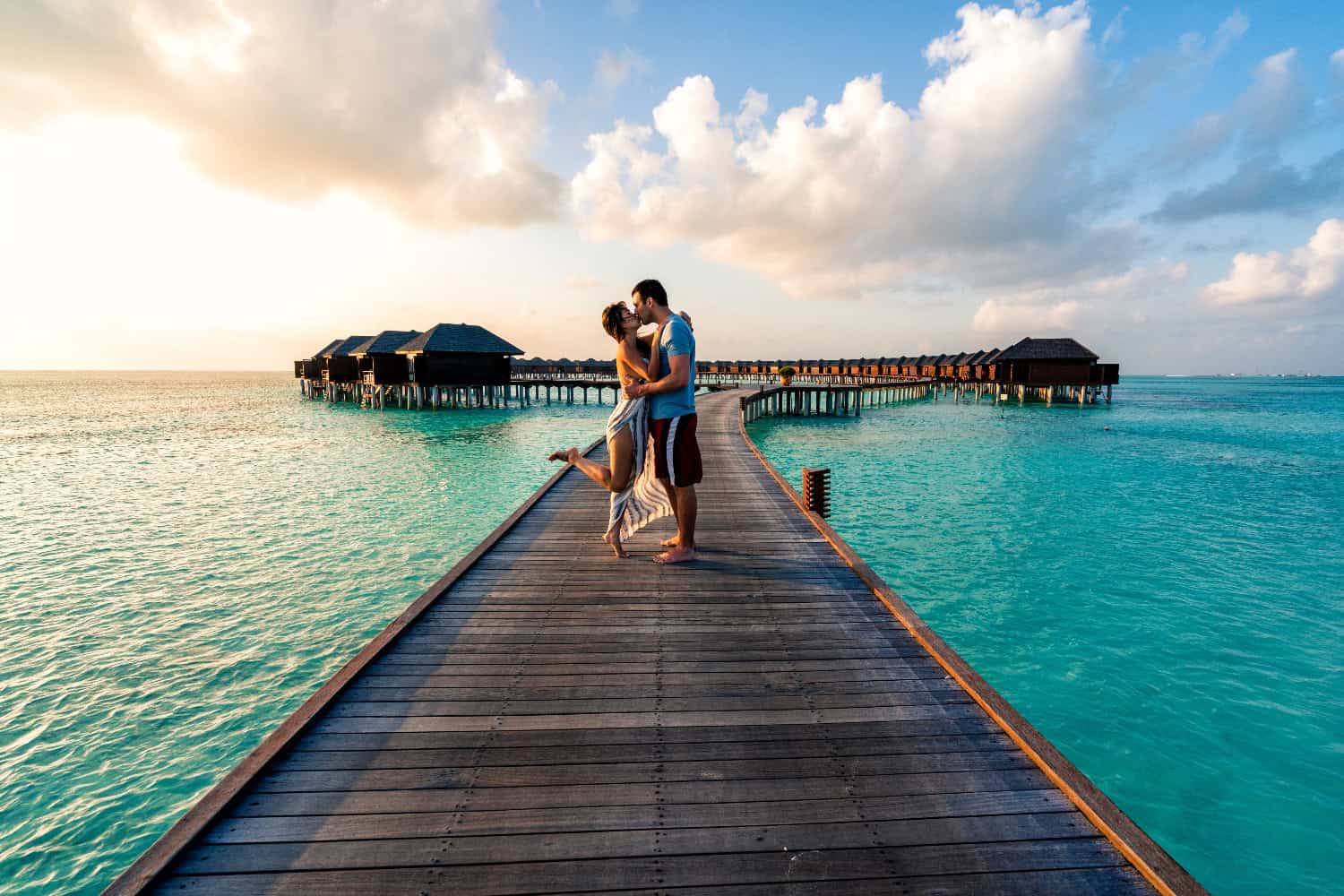 Ein Paar küsst sich auf einem Steg auf dem Wasser, Wasserbungalows im Hintergrund