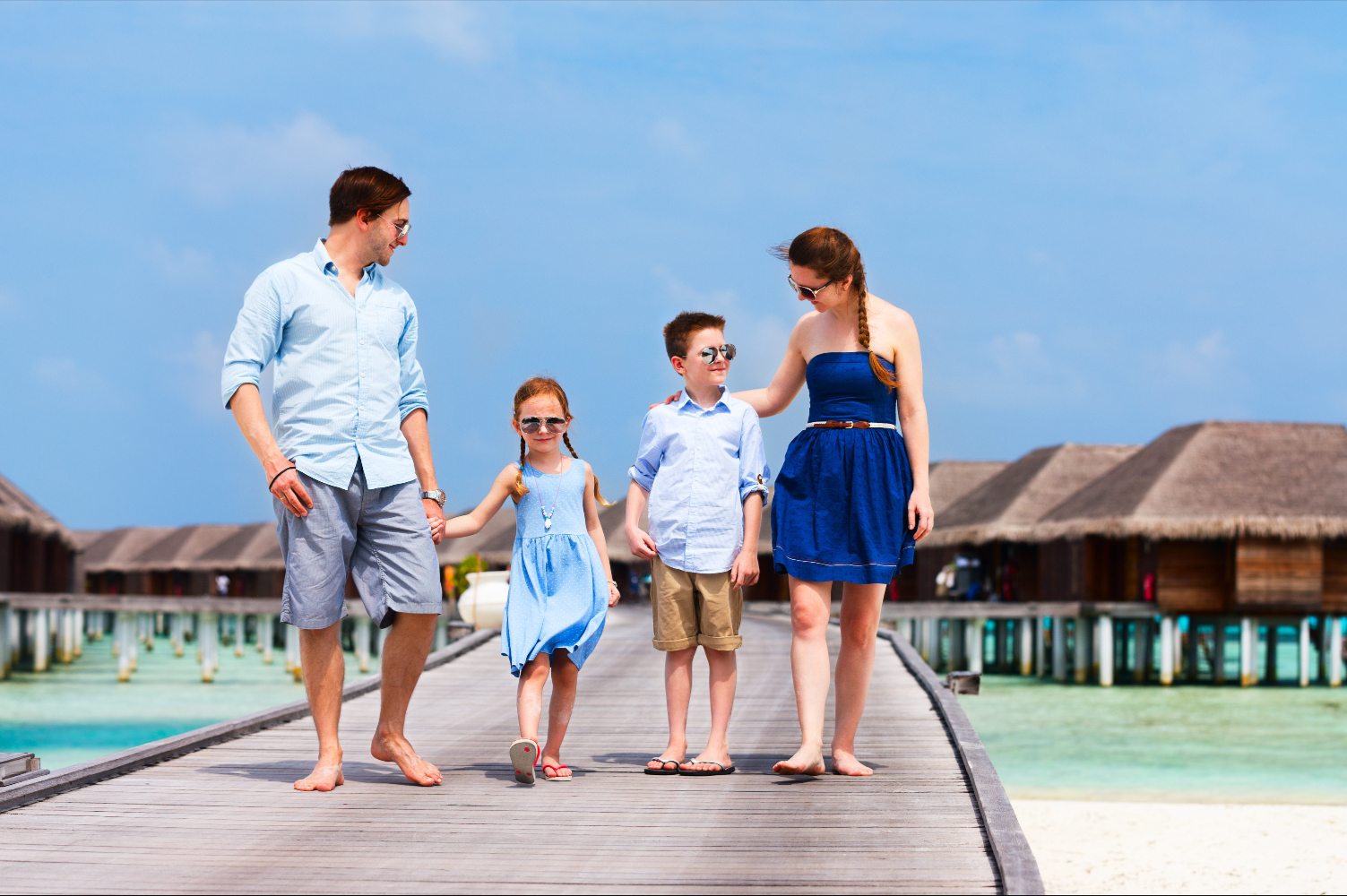 Familie mit zwei Kindern läuft über Holzsteg bei Wasserbungalows auf den Malediven