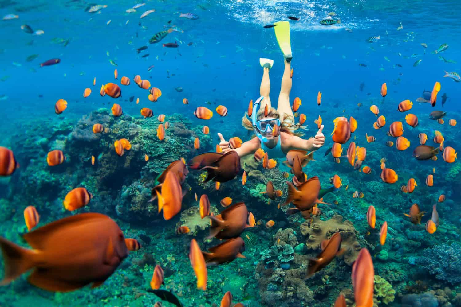 Frau beim Schnorcheln im türkisblauen Meer der Malediven, umgeben von bunten tropischen Fischen und Korallenriff