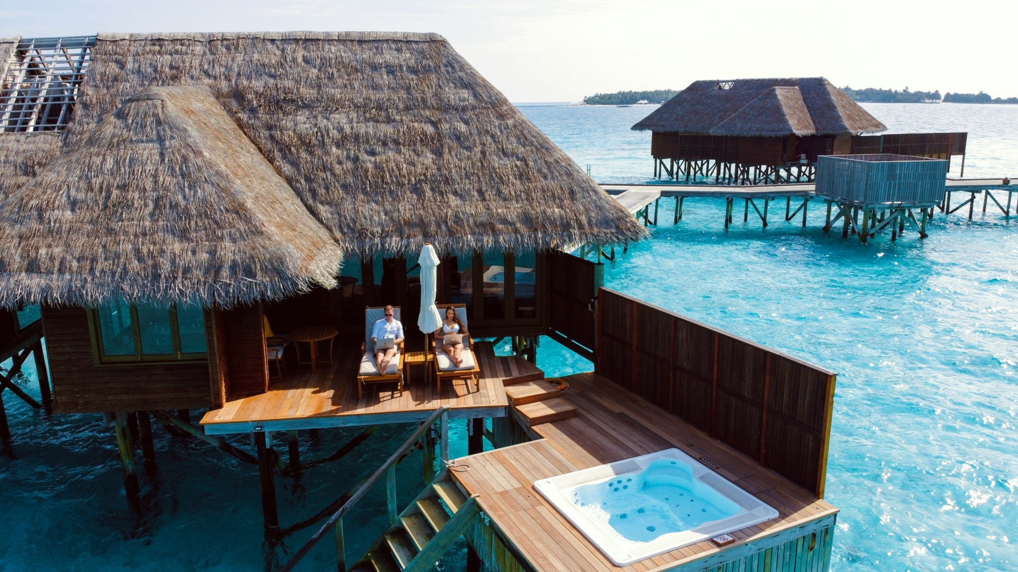 Paar entspannt auf der Terrasse eines Wasserbungalows mit privatem Pool über dem Meer auf den Malediven