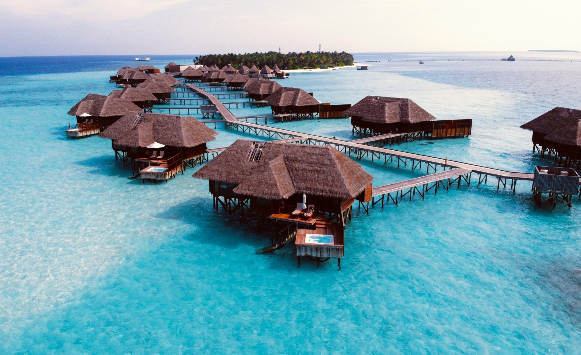 Wasserbungalows auf den Malediven verteilen sich über eine türkisfarbene Lagune mit Stegen und Insel im Hintergrund