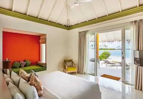 Helles Schlafzimmer mit Sitznische und direktem Zugang zur Terrasse mit Meerblick im Sun Siyam Olhuveli.
