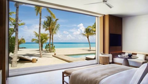 Schlafbereich der Beach Pool Villa mit bodentiefer Fensterfront und Blick auf weißen Sandstrand und türkisfarbene Lagune